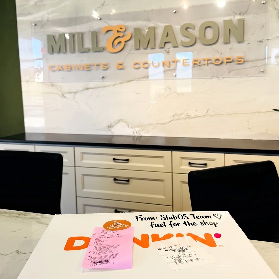 A Dunkin&rsquo; box on the counter at Mill & Mason Cabinets & Countertops, hand-labelled &lsquo;From: SlabOS Team, fuel for the shop&rsquo;.