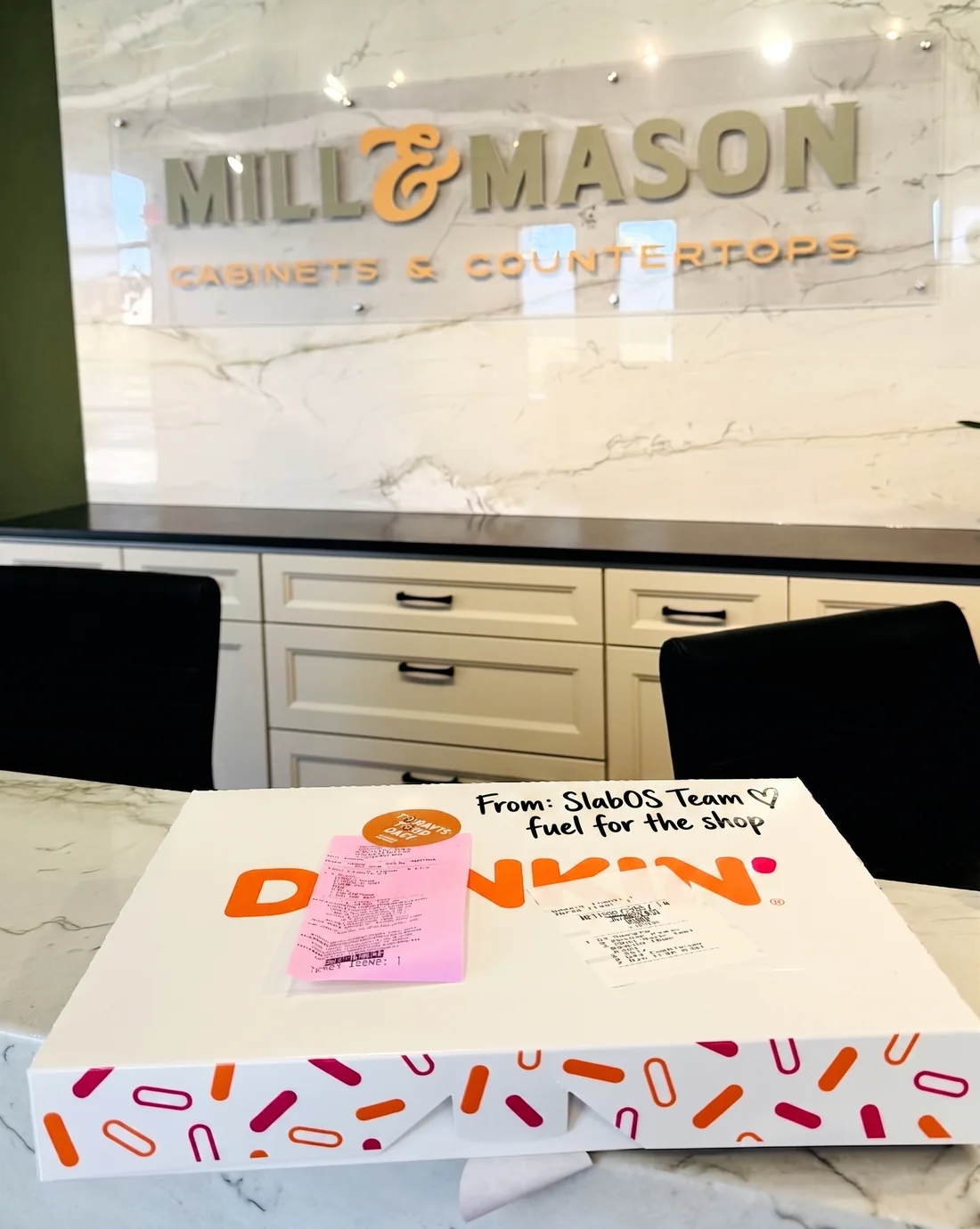 A Dunkin&rsquo; box on the counter at Mill & Mason Cabinets & Countertops, hand-labelled &lsquo;From: SlabOS Team, fuel for the shop&rsquo;.